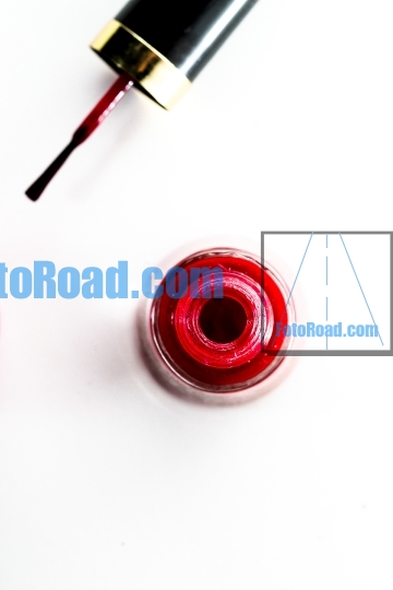 An opened bottle of red nail polish on white background table to