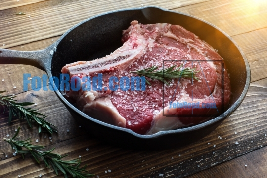Beef steak bone in inside iron skillet with rosemary and sea sal