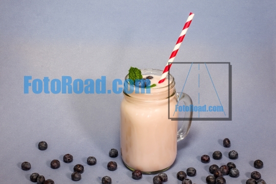 Blueberry smoothie with blueberry, mint leaf and straw on blue b