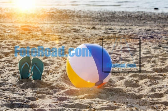 Flip flops on beach sand with colorful beach ball and sunbeam