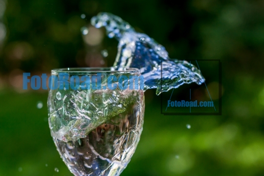 Hand holding glass with water splash outdoor with green ci back