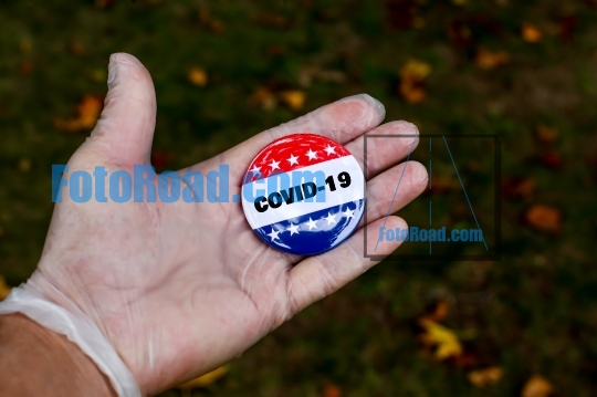 Hand with protective glove showing vote pin button with COVID-19