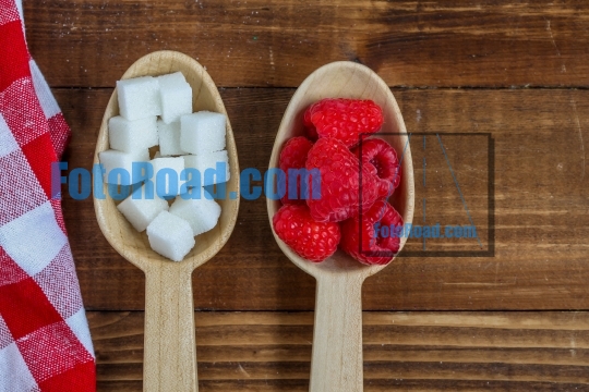 Healthy raspberries and uhealthy sugar in wooden spoons on woode