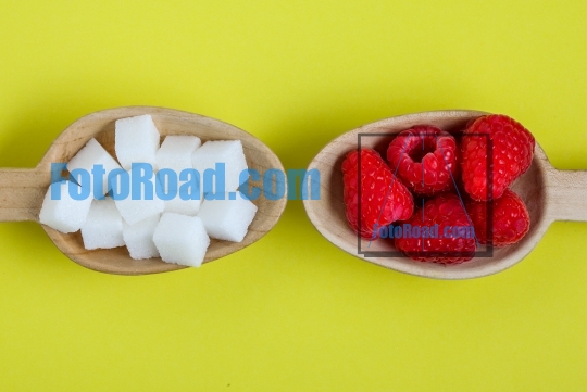 Healthy raspberries and unhealthy sugar in wooden spoons on yell