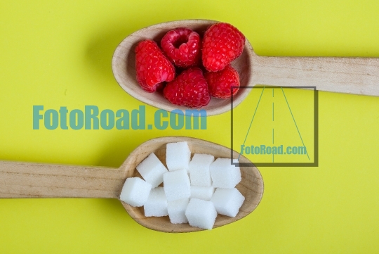 Healthy raspberries and unhealthy sugar in wooden spoons on yell