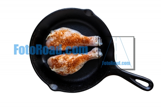 Iron skillet with chicken leggs and seasoning isolated on white 