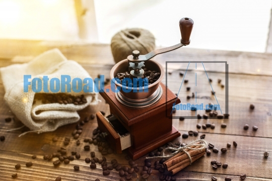 Manual coffee grinder on wooden table with sunny window behind  