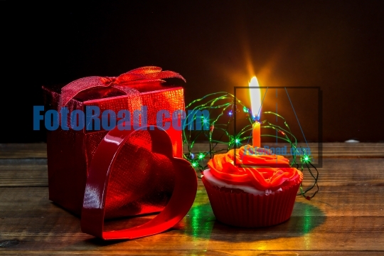 Red gift box with heart,  cup cake and candle on wooden table