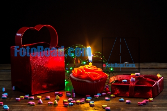 Red gift box with heart,  cup cake and candle on wooden table
