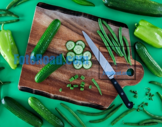 Sliced cucumber on cutting board with knife and other green vege