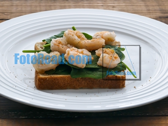 Toast with baby spinach and shrimps on plate