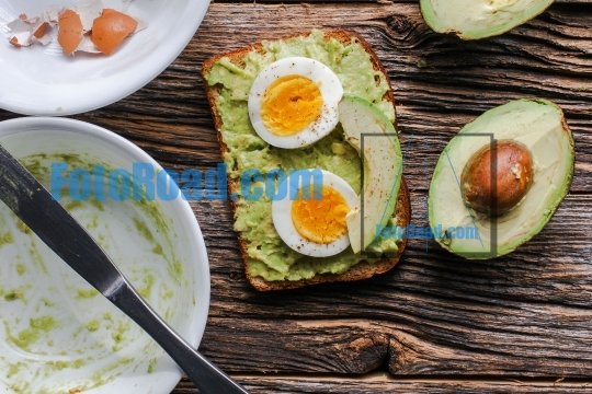Toast with mashed avocado and eggs on messy rustic wooden table 