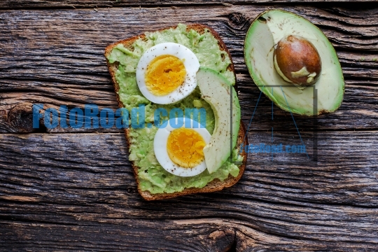 Toast with mashed avocado and eggs on rustic wooden table with  