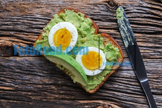 Toast with mashed avocado and eggs on rustic wooden table with k