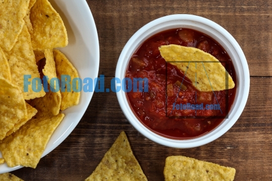 Tortilla chips inside bowl with salsa on rustic wooden table