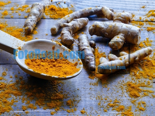 Turmeric roots and  powder in wooden spoon on wooden rustic look