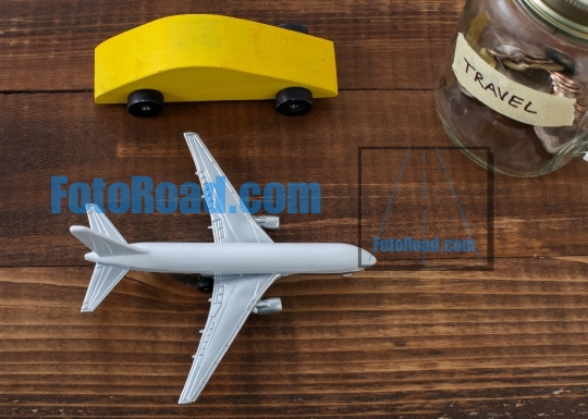 Wooden car with airplane and coins in jar with travel label on w