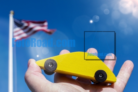 Yellow wooden car holding against blue sky with american flag an