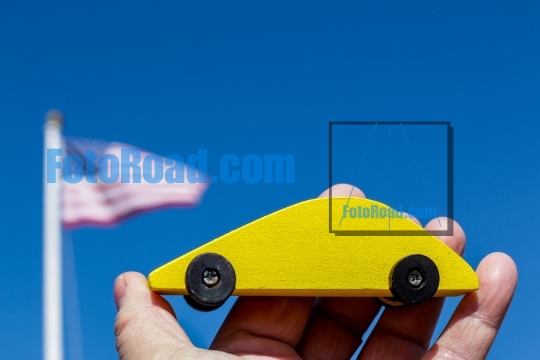 Yellow wooden car holding in hand against blue sky with american