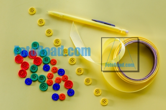 Multicolored buttons, yellow bow and yellow pencil on yellow bac