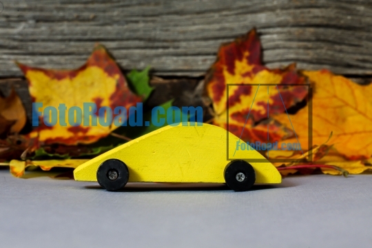 Yellow wooden toy car with cloorful leaves 